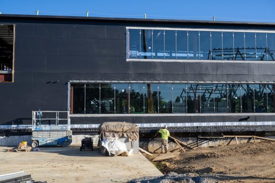 an unfinished new construction building with black paneling sitting on a dirt and concrete slab